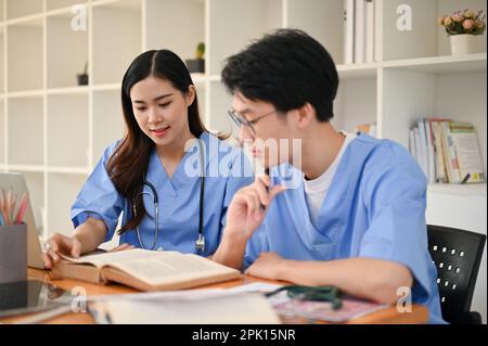 Attraktive junge asiatische Medizinstudentin, die mit ihrer Freundin in der Bibliothek studiert und sich auf die Prüfung vorbereitet. Stockfoto