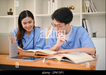 Kluger junger asiatischer Medizinstudent, der seinen Freund in der Bibliothek studiert und unterrichtet. Stockfoto