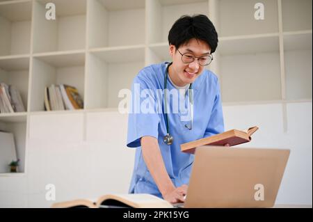 Smart junger asiatischer männlicher Medizinstudent lehnt sich auf den Tisch, mit Laptop, recherchieren medizinisches Papier im Internet. Stockfoto