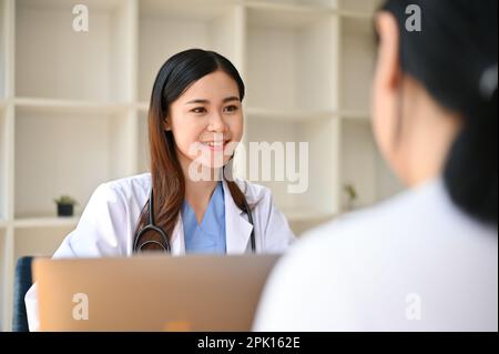 Professionelle und freundliche Millenialasiatische Ärztin berät sich mit einem Patienten im Untersuchungsraum des Krankenhauses über einen medizinischen Behandlungsplan. Stockfoto