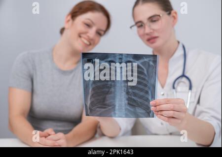 Der Arzt konsultiert eine kaukasische Frau und kommentiert die Röntgenaufnahme der Lunge. Stockfoto