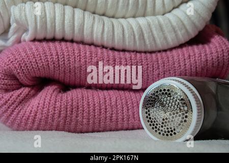 Anti-Pilling-Rasierer. Gerät zum Rasieren von Kleidung. Anti-Plush-Rasierer. Elektrischer tragbarer Pullover, Pille, Entfärbung, Fusselentferner aus pinkfarbenem Acryl- oder Wollpullover. Elektrorasierer nach der Reinigung und aufgefangenen Fusseln. Ein Pullover aus der Nahaufnahme. Alte gebrauchte Kleidung mit Pillen. Stockfoto