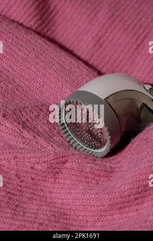 Anti-Pilling-Rasierer. Gerät zum Rasieren von Kleidung. Anti-Plush-Rasierer. Elektrischer tragbarer Pullover, Pille, Entfärbung, Fusselentferner aus pinkfarbenem Acryl- oder Wollpullover. Elektrorasierer nach der Reinigung und aufgefangenen Fusseln. Ein Pullover aus der Nahaufnahme. Alte gebrauchte Kleidung mit Pillen. Stockfoto
