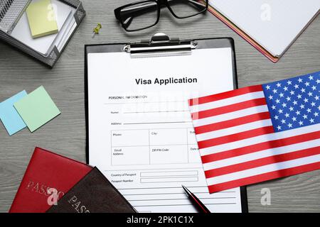 Visumantrag, amerikanische Flagge, Pässe und Schreibwaren auf Holztisch, flach liegend Stockfoto