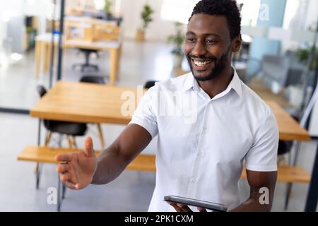 Glücklicher afroamerikanischer Gelegenheitsunternehmer, der über die Arbeit diskutiert und ein Notebook in einem modernen Büro verwendet Stockfoto