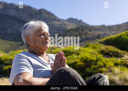 Glückliche ältere, birassische Frau, die Yoga macht und in den Bergen meditiert Stockfoto