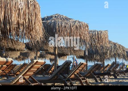 Wunderschöne Strohschirme und Holzliegen am Strand Stockfoto