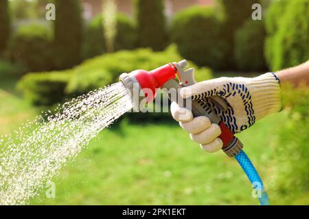 Mann, der Wasser aus dem Schlauch spritzt, im Garten, Nahaufnahme Stockfoto