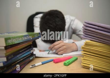 Dateifoto vom 05. April 03/17 eines Grundschullehrers, der neben einem Haufen von Klassenbüchern gestresst aussieht. Fast jeder fünfte Lehrer musste bei steigenden Lebenshaltungskosten einen zweiten Arbeitsplatz annehmen, so eine Umfrage. Ausgabedatum: Mittwoch, 5. April 2023. Stockfoto