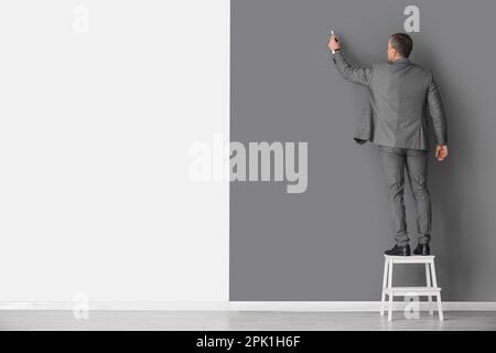 Erfahrener Unternehmensberater mit Markierung auf der Trittleiter in der Nähe der Schwarzweißwand, Rückansicht Stockfoto