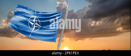 Die Flagge der NATO winkt im Wind auf einem Fahnenmast gegen den Himmel Stockfoto