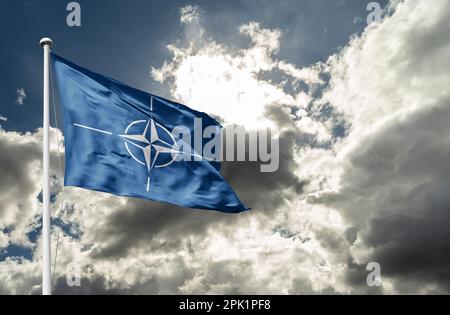 Die Flagge der NATO winkt im Wind auf einem Fahnenmast gegen den Himmel Stockfoto