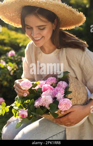 Eine junge Frau hält einen Korb mit wunderschönen Teerösen im Garten, Nahaufnahme Stockfoto