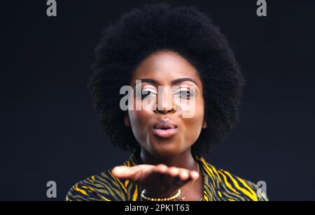 Liebe auf deine Art zu senden. Eine junge Frau, die vor einem dunklen Hintergrund einen Kuss geblasen hat. Stockfoto