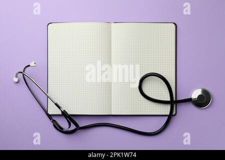 Offenes Notebook und Stethoskop auf violettem Hintergrund, flach liegend. Platz für Text Stockfoto