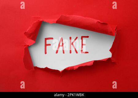 Wort Fake auf weißem Hintergrund, Blick durch das Loch in rotem Papierriss Stockfoto