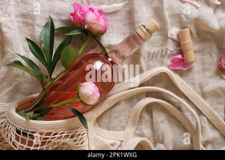Flache Laienzusammensetzung mit Rosenwein, Netzbeutel und wunderschönen Pfingstrosen auf weißem Stoff Stockfoto