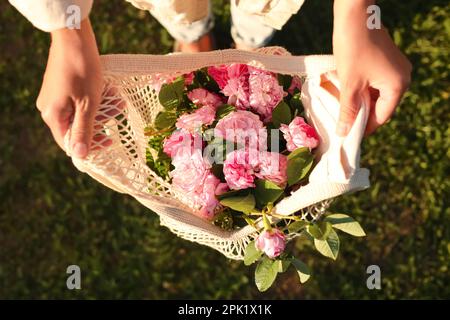 Frau mit Netzbeutel und wunderschönen Teerösen im Freien, Draufsicht Stockfoto