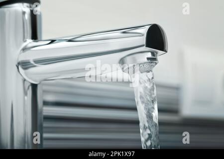 Wasser fließt aus dem Hahn auf verschwommenem Hintergrund, Nahaufnahme Stockfoto