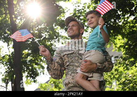 Soldat und sein kleiner Sohn mit amerikanischen Flaggen draußen, Blick aus dem niedrigen Winkel. Veteranentag in den USA Stockfoto