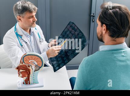 Arzt erklärt dem männlichen Patienten die Ergebnisse der MRT-Untersuchung seines Gehirns. Diagnostik von Krankheiten und Kopfverletzungen Stockfoto