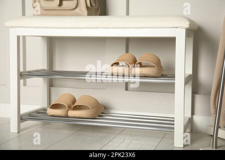 Aufbewahrungsbank mit Paar Gummipantoffeln in der Nähe der weißen Wand im Zimmer Stockfoto