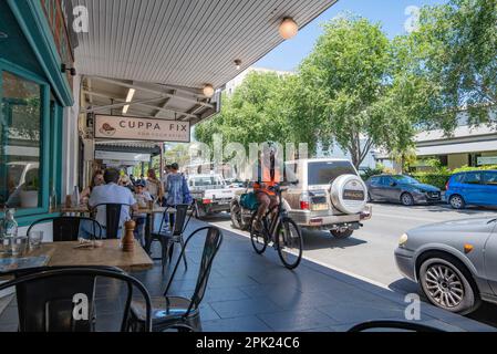 Gäste können auf dem Fußweg (Bürgersteig) im Freien speisen, während ein Uber-Fahrradfahrer in Glebe, New South Wales, Australien vorbeifährt Stockfoto