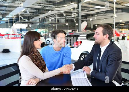 Junges Paar beim Kauf eines neuen Autos im Showroom des Autohauses - Signatur Kaufvertrag mit dem Verkäufer Stockfoto