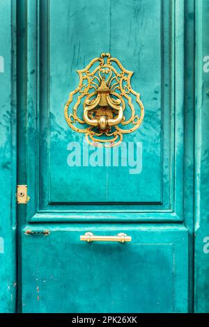 Ein alter goldener Türklopfer im Vintage-Stil an einer hellblauen türkisfarbenen Tür in Frankreich Stockfoto