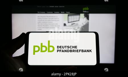 Person, die ein Smartphone mit dem Logo der Deutschen Pfandbriefbank AG (PBB) auf dem Bildschirm vor der Website hält. Konzentrieren Sie sich auf das Display des Telefons. Stockfoto