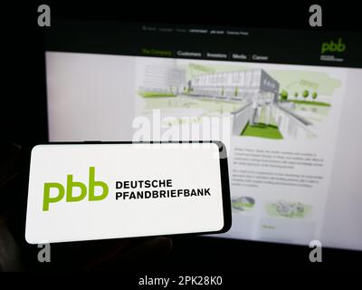 Person, die ein Mobiltelefon mit dem Logo der Deutschen Pfandbriefbank AG (PBB) auf dem Bildschirm vor der Unternehmenswebseite hält. Konzentrieren Sie sich auf das Display des Telefons. Stockfoto