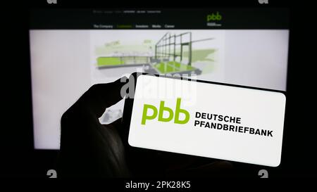 Person, die ein Mobiltelefon mit dem Logo der Deutschen Pfandbriefbank AG (PBB) auf dem Bildschirm vor der Unternehmenswebseite hält. Konzentrieren Sie sich auf das Display des Telefons. Stockfoto