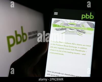 Person, die ein Smartphone mit einer Website der Deutschen Pfandbriefbank AG (PBB) auf dem Bildschirm vor dem Logo hält. Konzentrieren Sie sich auf die Mitte des Telefondisplays. Stockfoto