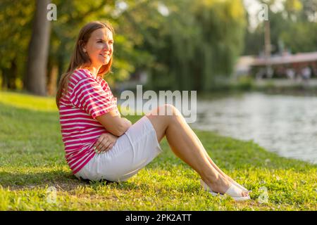 Wunderschöne Frau, die sich ausruht und sich auf dem Gras in einem Park ausruht Stockfoto