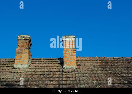 Roter Backsteinkamin oben im Dorfhaus. Ein Dach aus Fliesen am Hintergrund des Himmels. Stockfoto