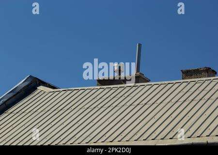 Metalldach eines Einzelhauses und Schornstein am Himmel, Dachziegel aus Metall, Dachrinnen. Stockfoto