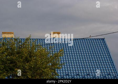 Metalldach eines Einzelhauses und Schornstein am Himmel, Dachziegel aus Metall, Dachrinnen. Stockfoto