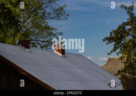 Metalldach eines Einzelhauses und Schornstein am Himmel, Dachziegel aus Metall, Dachrinnen. Stockfoto