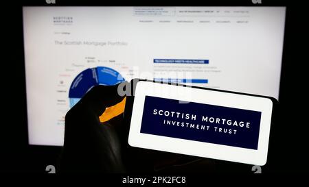 Person, die ein Mobiltelefon mit dem Logo von Scottish Mortgage Investment Trust plc auf dem Bildschirm vor der Unternehmenswebseite hält. Konzentrieren Sie sich auf das Display des Telefons. Stockfoto