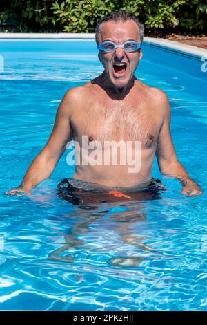 Ein weißer Mann mittleren Alters jubelt, während er teilweise in einem Swimmingpool mit Schwimmbrille tauchte Stockfoto