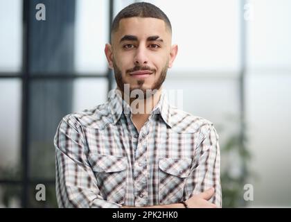 Junger, gutaussehender Geschäftsmann, der im Amt mit gekreuzten Armen steht. Stockfoto