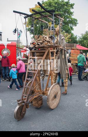 Eine Person auf Stelzen mit einem mobilen Gerät, das einen feuerspeienden Drachen trägt, wie sie etwa 2015 beim Skipton International Puppet Festival zu sehen ist. Stockfoto