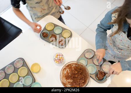 Zwei Kinder schöpfen Schokoladenmischung aus Maisflake und machen zu Ostern Schokoladennester aus Mini-Eiern Stockfoto