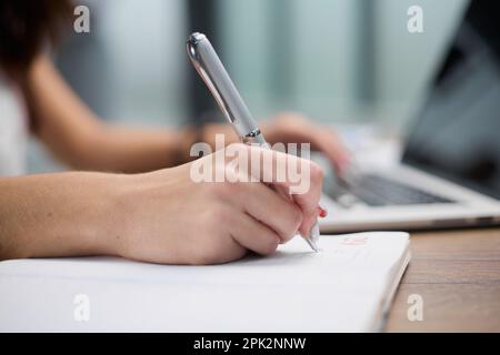Nahaufnahme männlicher Hände, die in einem Notizbuch auf einem Tisch mit verschiedenen Gegenständen schreiben Stockfoto
