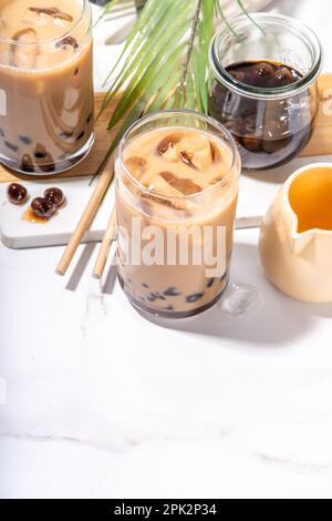 Iced Tapica Coffee Latte oder boba Pearl Bubbles Milchtee, asiatisches trendiges kaltes Kaffeegetränk mit Tapiokasseln und zerstoßenem Eis, auf weißem Marmorhintergrund Stockfoto