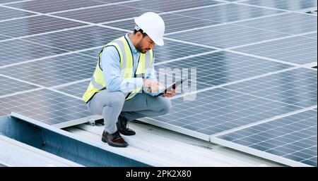 Junger Ingenieur oder Auftragnehmer, der Solarpaneele auf einem Dach in der Stadt inspiziert. Ein selbstbewusster junger Manager oder Wartungsmitarbeiter, der während der Installation lächelt Stockfoto