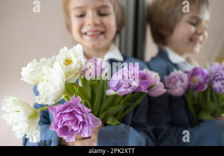 Wunderschöner Strauß aus weißen und lila Tulpen im Vordergrund, das Gesicht eines süßen, lächelnden Jungen in Unschärfe-Richtung neben dem Spiegel. Muttertag, Valentinstag, Bir Stockfoto