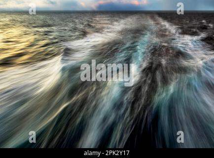 Die Kraft der Wellen bei langer Exposition, verschwommenes Wasser, die Beleuchtung der Meeresoberfläche bei Sonnenuntergang. Stockfoto