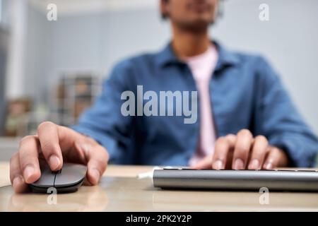 Nahaufnahme eines jungen schwarzen Mannes, der am Schreibtisch des Colleges Computer benutzt, mit Schwerpunkt auf männlichen Händen, die tippen und Maus benutzen Stockfoto