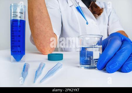 Wissenschaftler Arzt Pipettieren Proben im Labor mit vielen wissenschaftlichen Dingen - Becher, Zylinder, Pipette, Flüssigkeiten, Fläschchen, Ampulle, Ständer und mehr Stockfoto